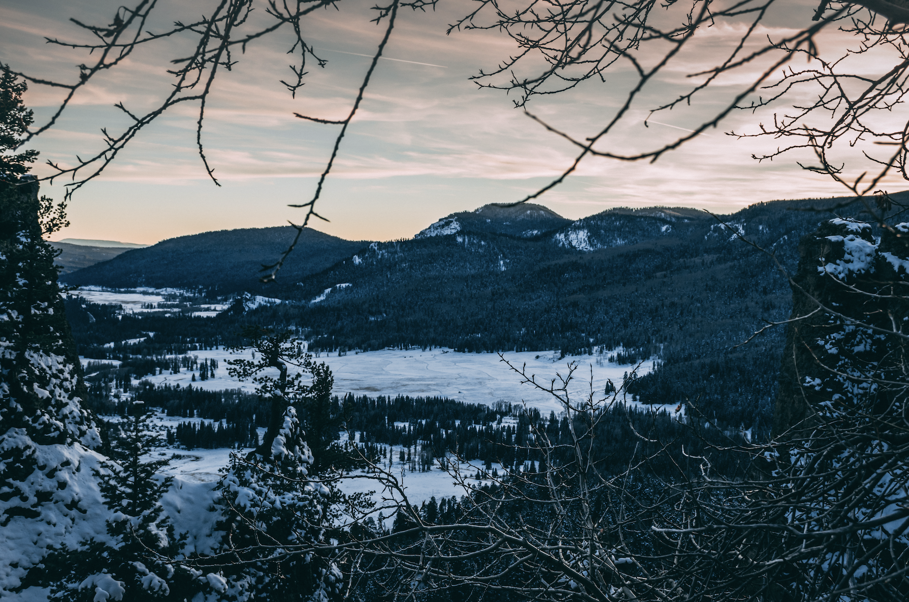 Looking through tree branches at snowy valley and dark tree-covered mountains