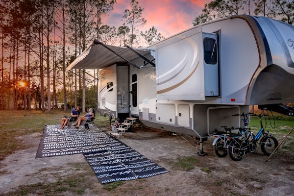 Cassie and Joshua Bailey sit in camp chairs next to their Highland Ridge Open Range Fifth Wheel at sunset.