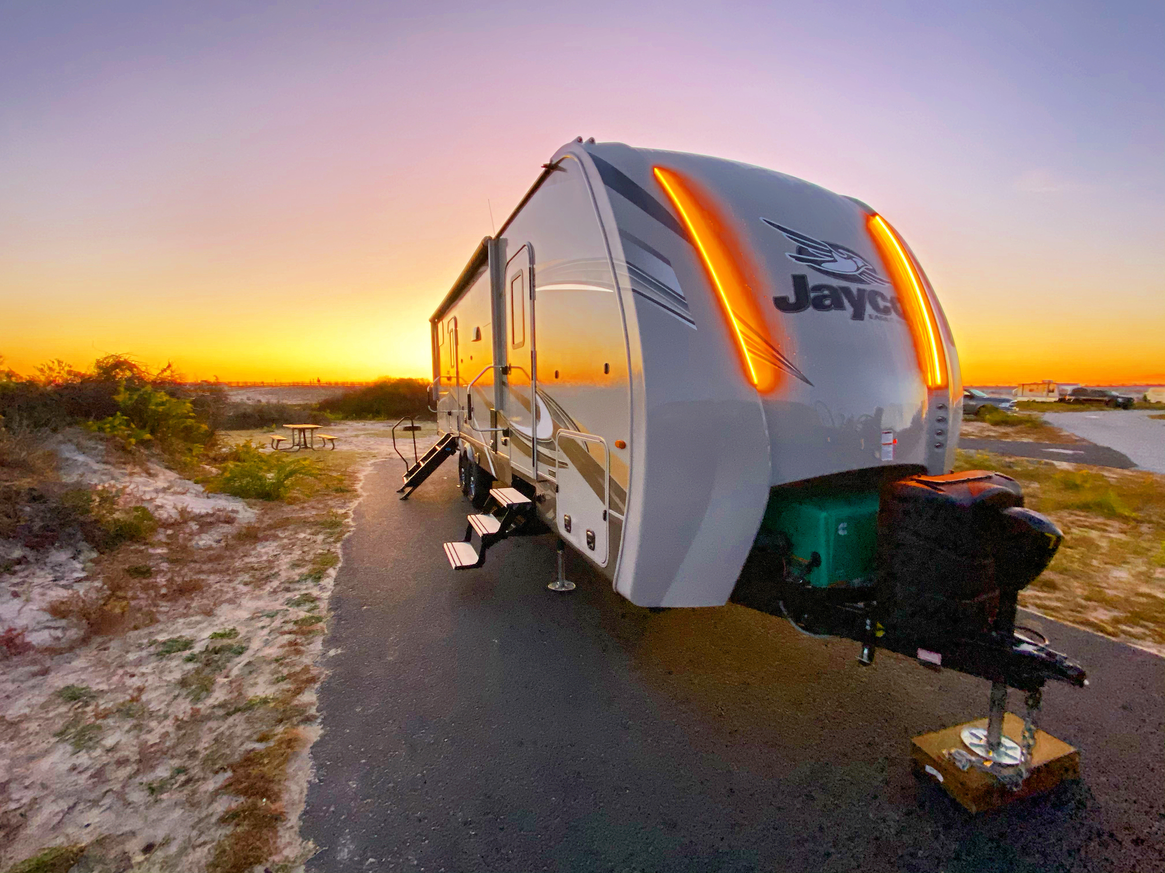 A Jayco RV trailer parked at a sandy campsite reflecting the sunrise. 