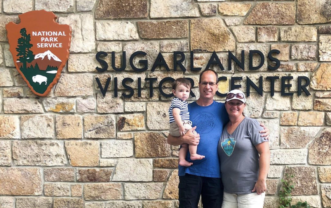 A middle aged couple holding their grandson at a national park visitor center. 