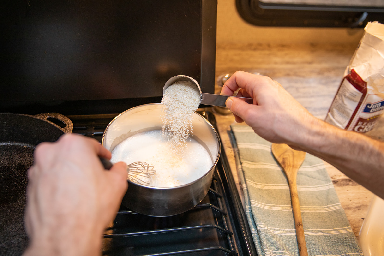 Stirring dry grits into hot liquid on the stove.