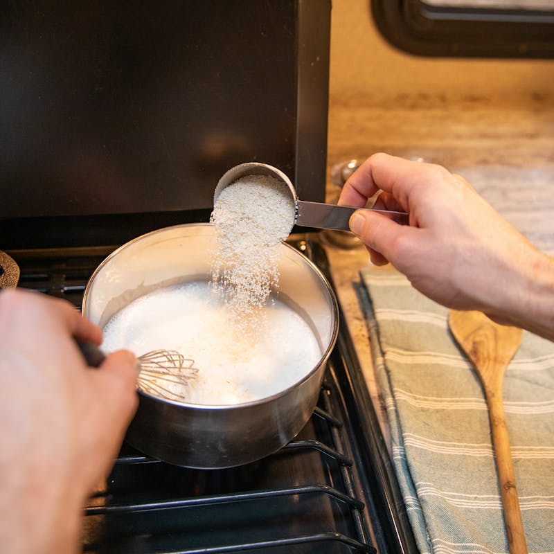 Stirring dry grits into hot liquid on the stove.