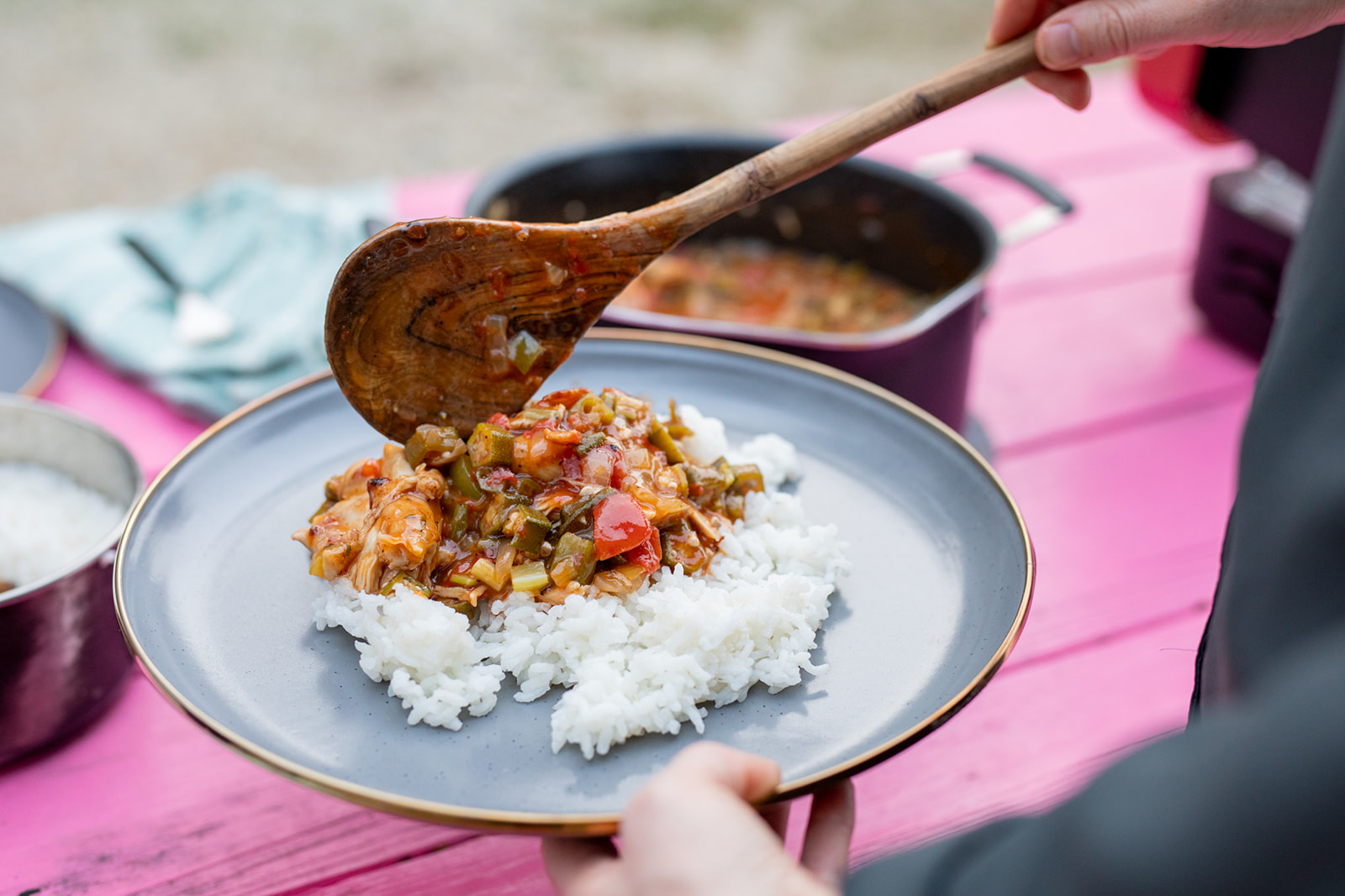 Spooning chicken and sauce over a plate of white rice. 