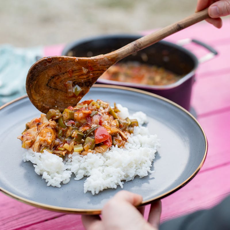 Spooning chicken and sauce over a plate of white rice.