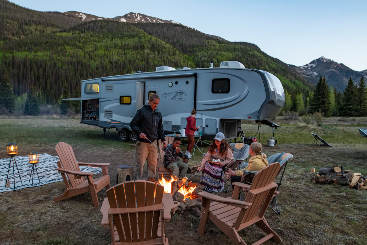 The Carew family sitting around a campfire roasting marshmallows in front of their RV at dusk