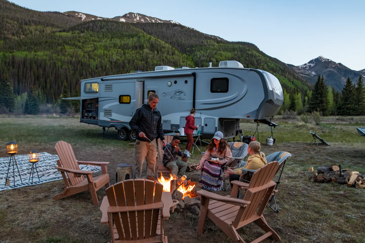 The Carew family sitting around a campfire roasting marshmallows in front of their RV at dusk
