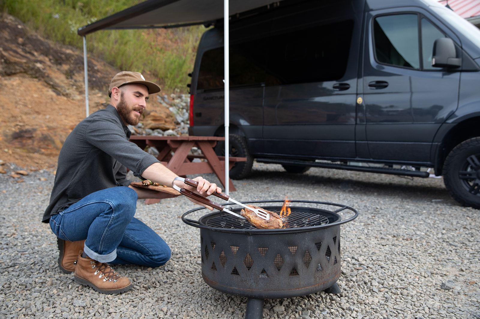 A man cooking Cornish hens over an open flame at a campsite.