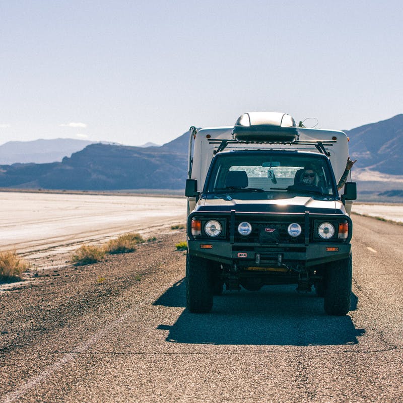 Blonde woman towing her trailer behind her, with her hand out the window, driving down a 2 lane road in the mountains.
