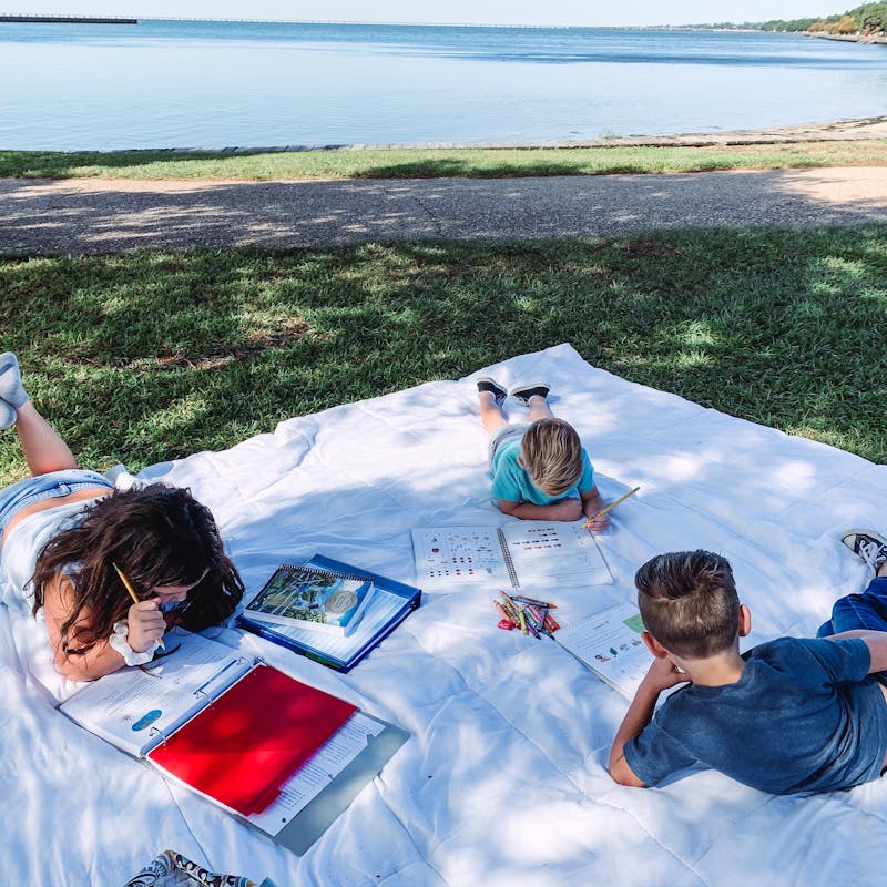 The Darren and Amanda Bone family sits on a blanket outside while reading and studying