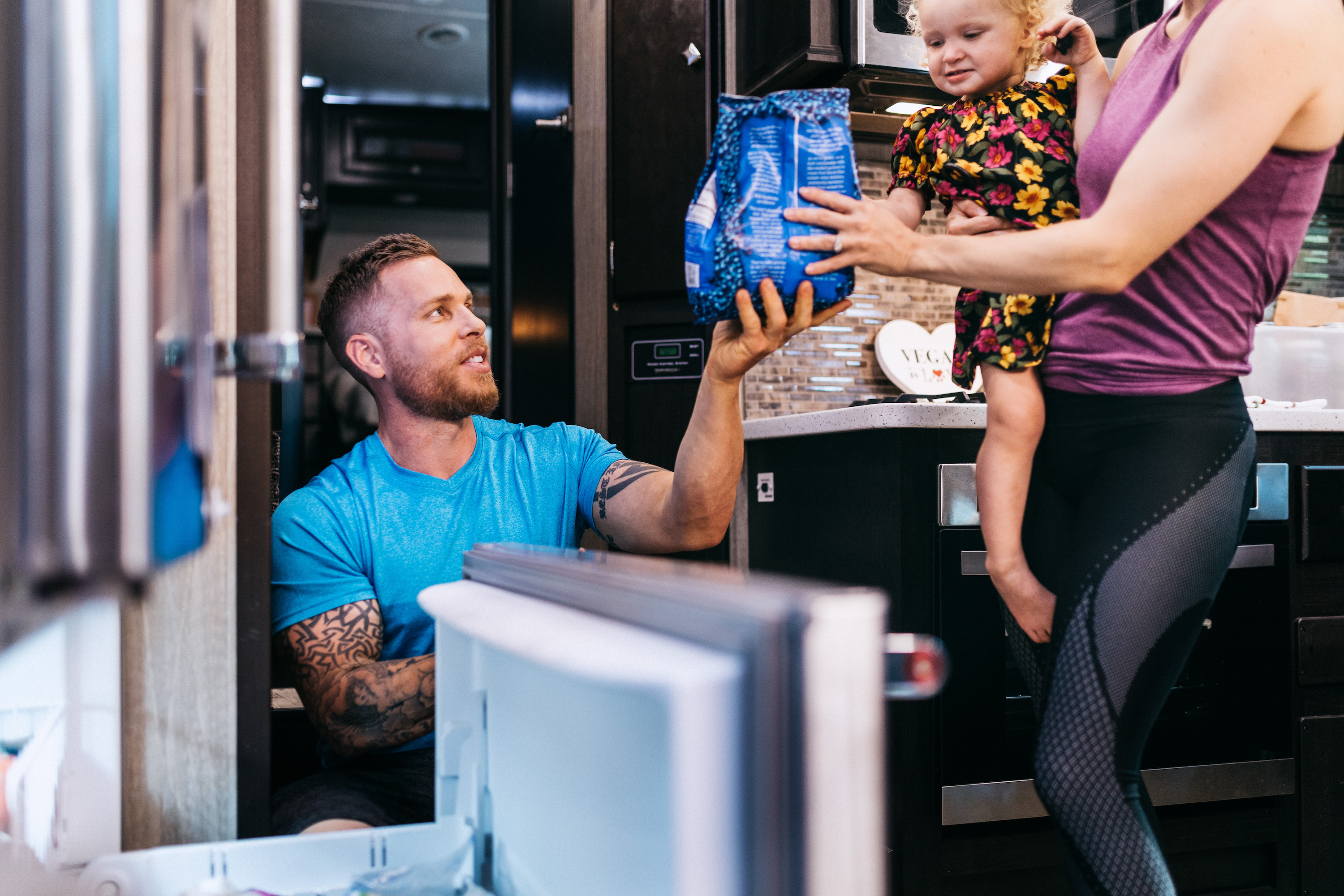 A man handing a bag of frozen blueberries to a young mother holding a child.