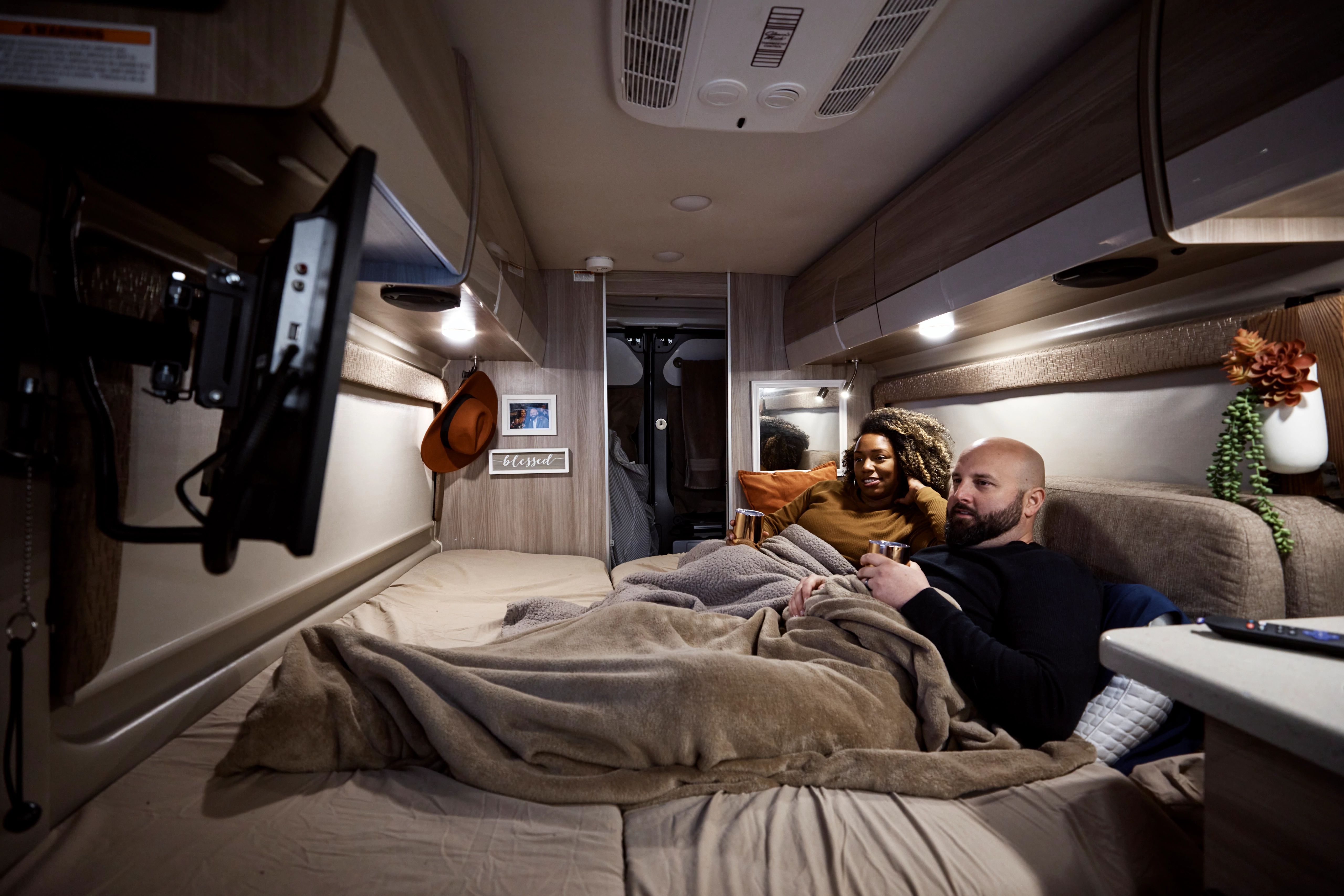 Gabe and Rocio Rivero lounge in the bed of their RV while they watch tv