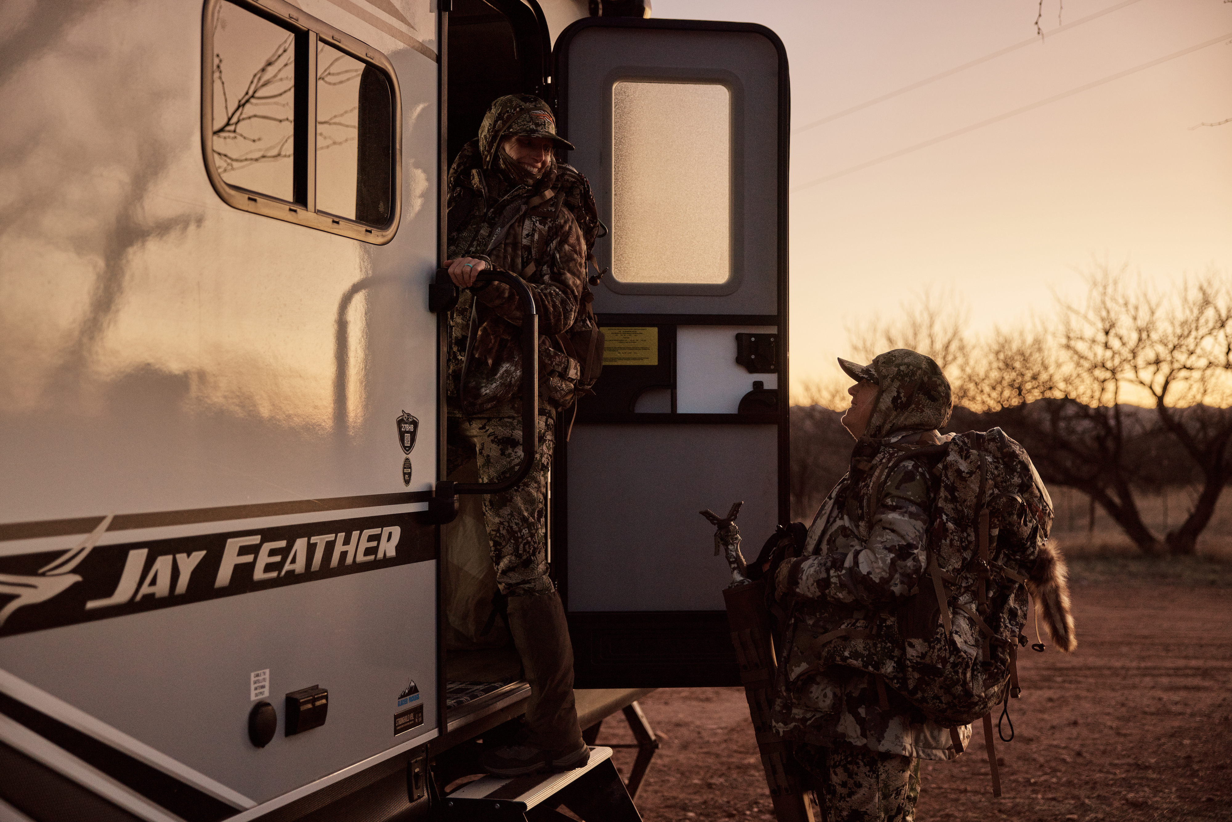 Two veteran women walking through the door of a Jayco Jay Feather RV after a hunt 