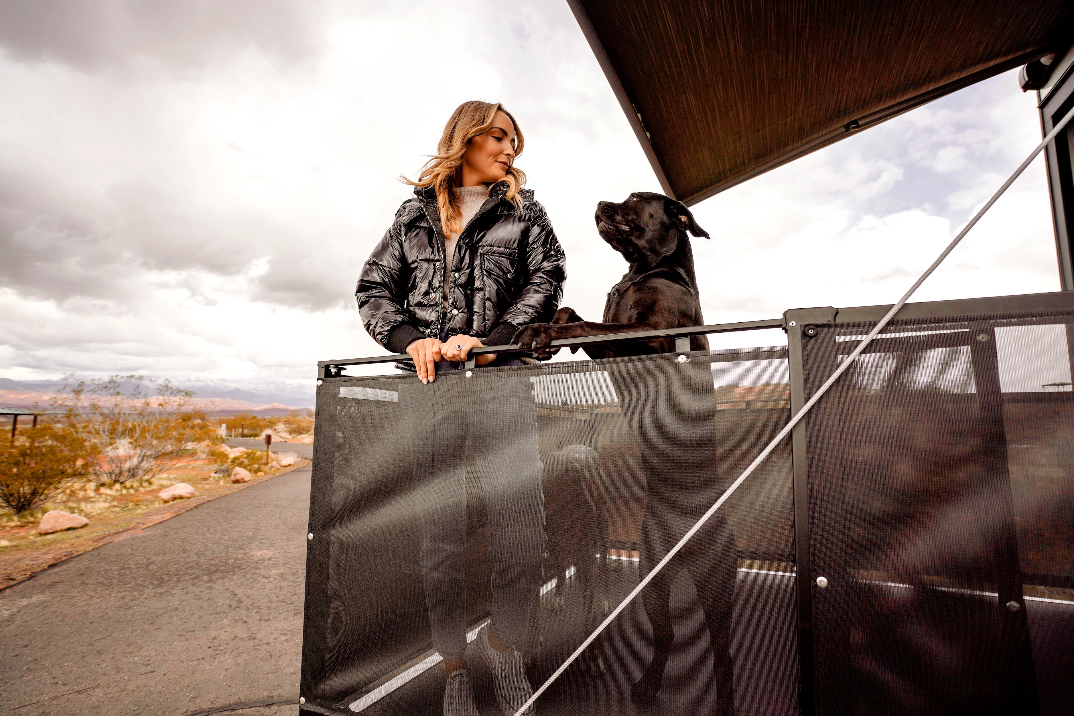 A woman stand on the porch of a toy hauler RV with her dog.