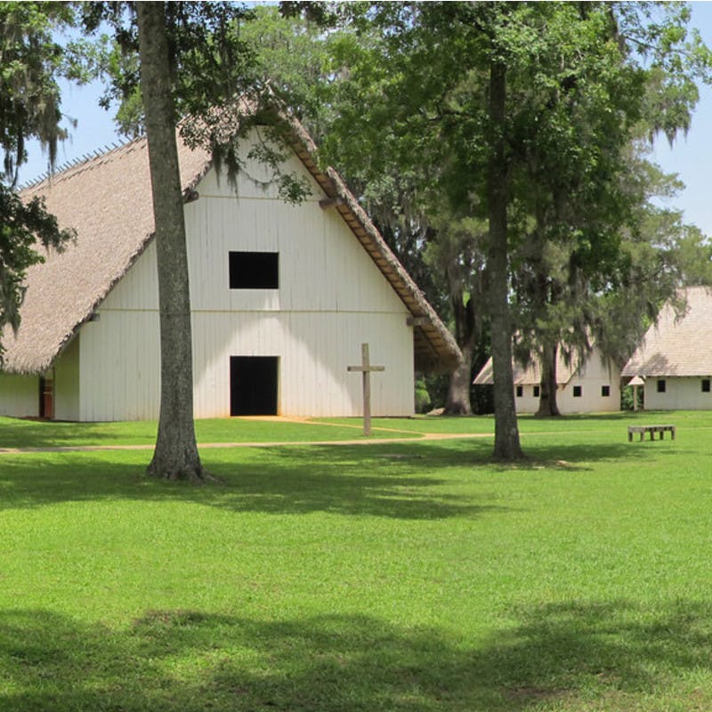 Mission San Luis with A-frame buildings, grass lawns, palm trees and wooden crosses in Tallahassee, Florida.