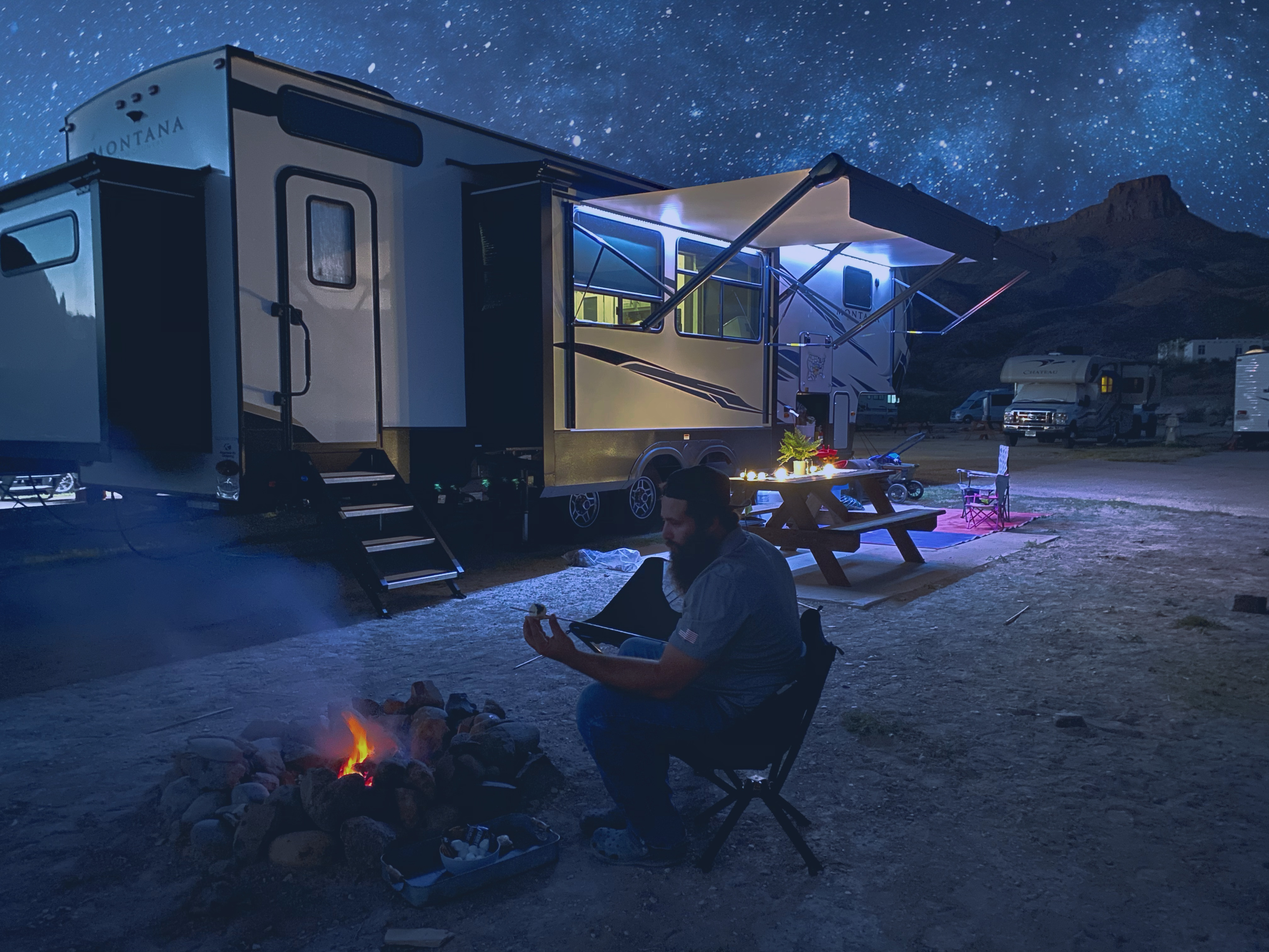 Sammy Seles's husband puts a marshmallow on a stick by a fire pit outside of their Keystone Montana under a starry sky.