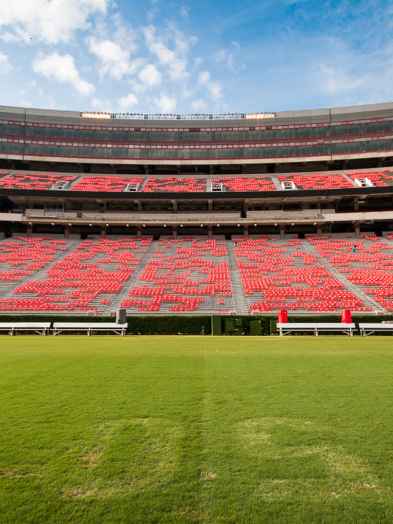 Football stadium, with red seats, and a green field at the 50 yard line.