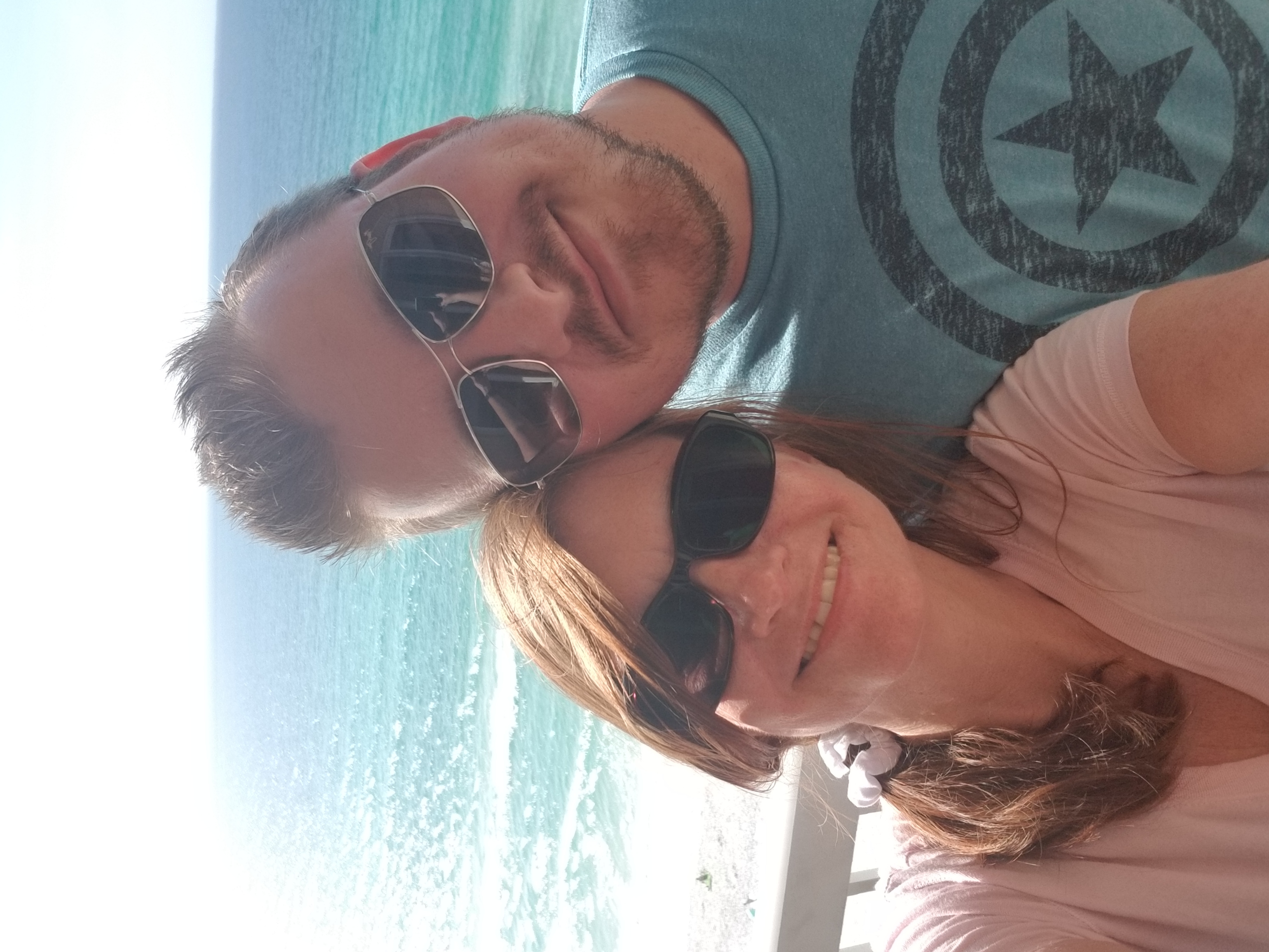 Julie and Brandon taking a selfie in front of the ocean wearing sunglasses.