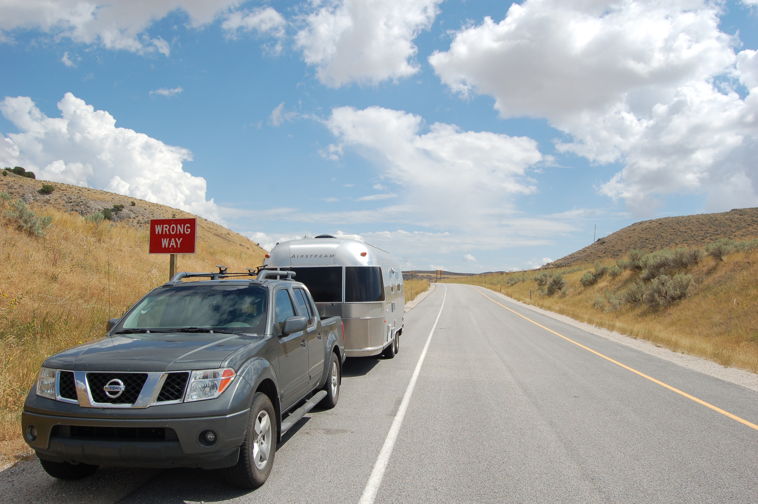 A car and an Airstream trailer parked on the side of a road on a beautiful day.