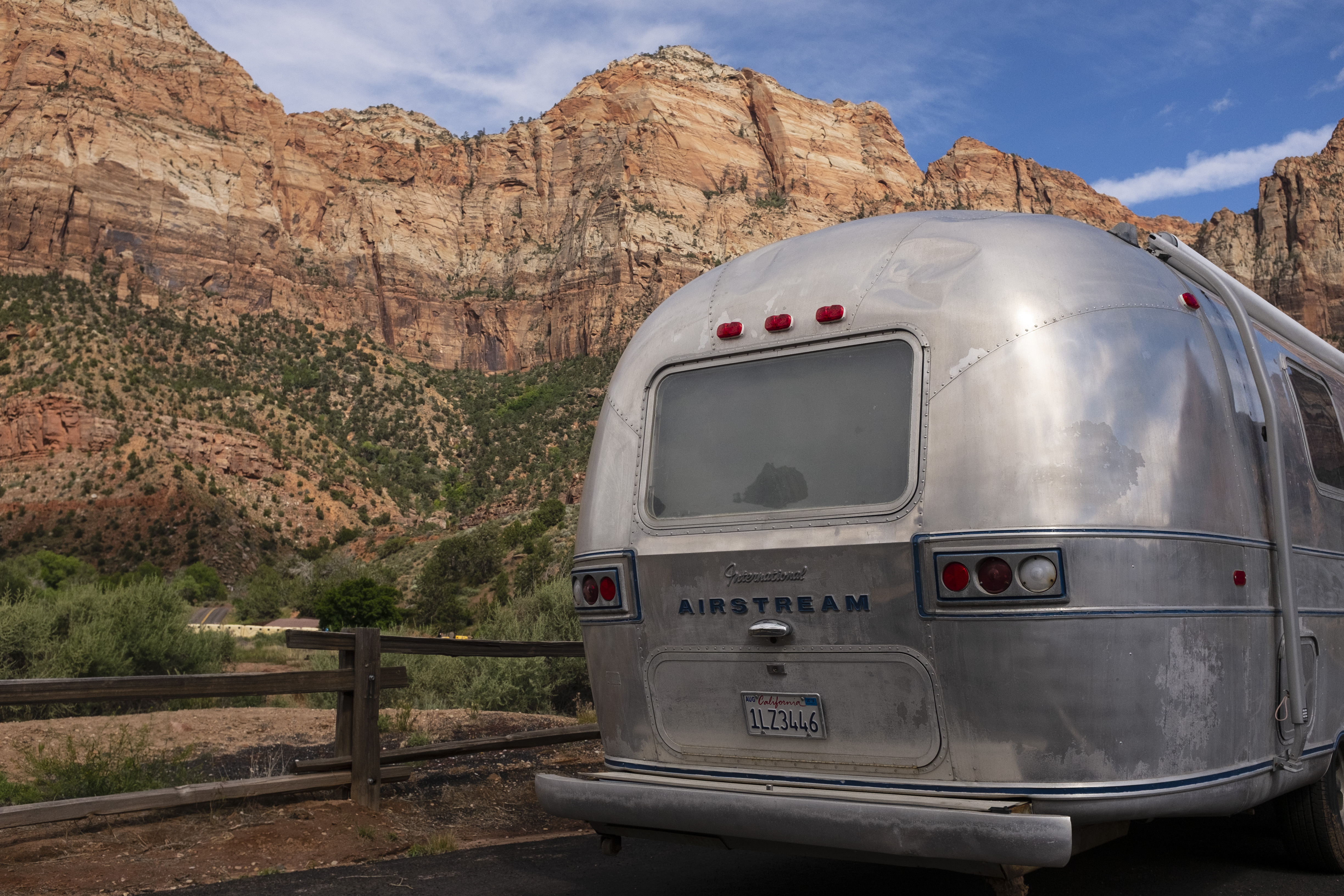A shot of the family RV on the road, in front of red rock cliffs.