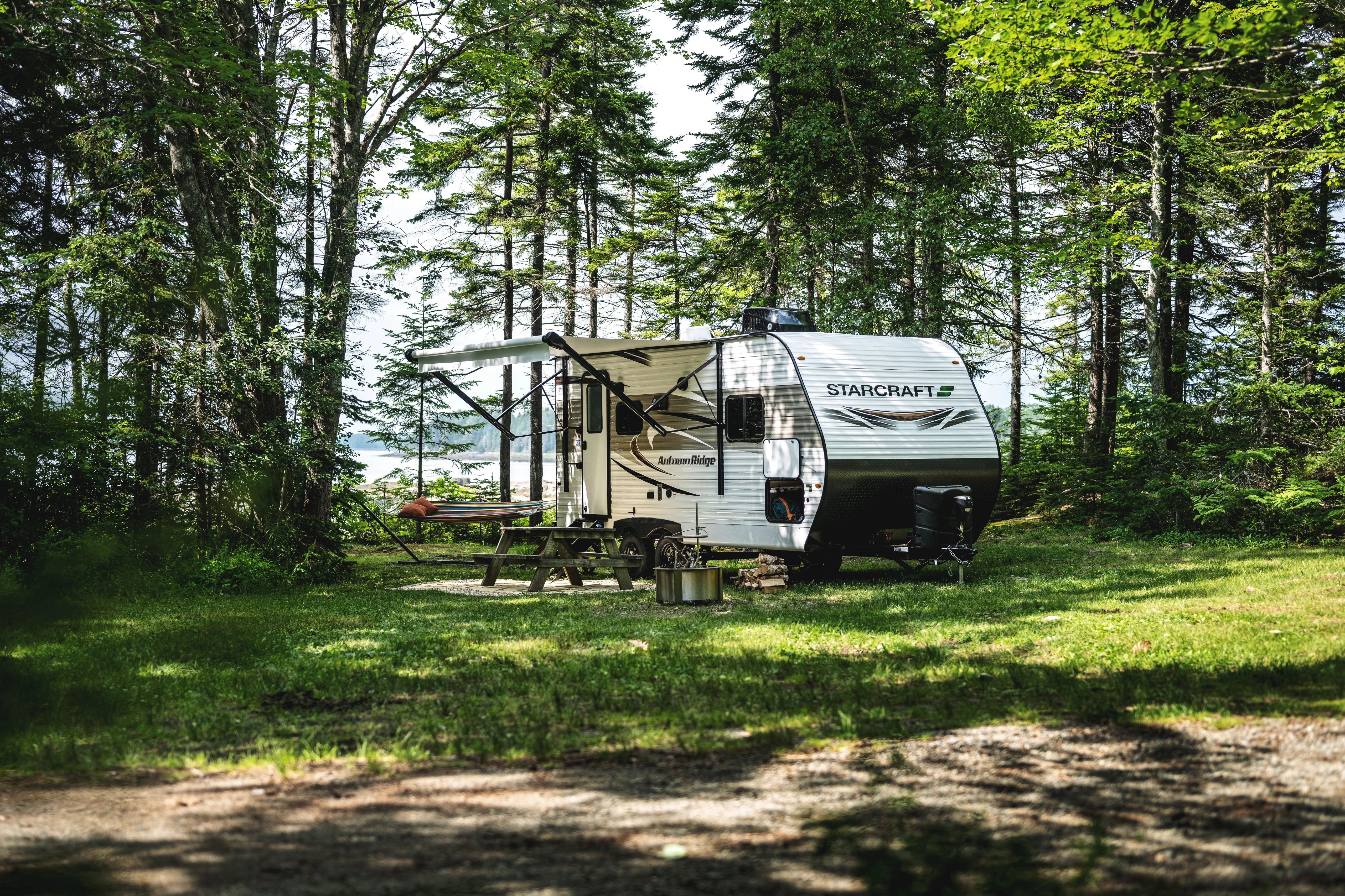 a starcraft lightweight travel travel parked at a campground near a picnic table and a lake in the distance