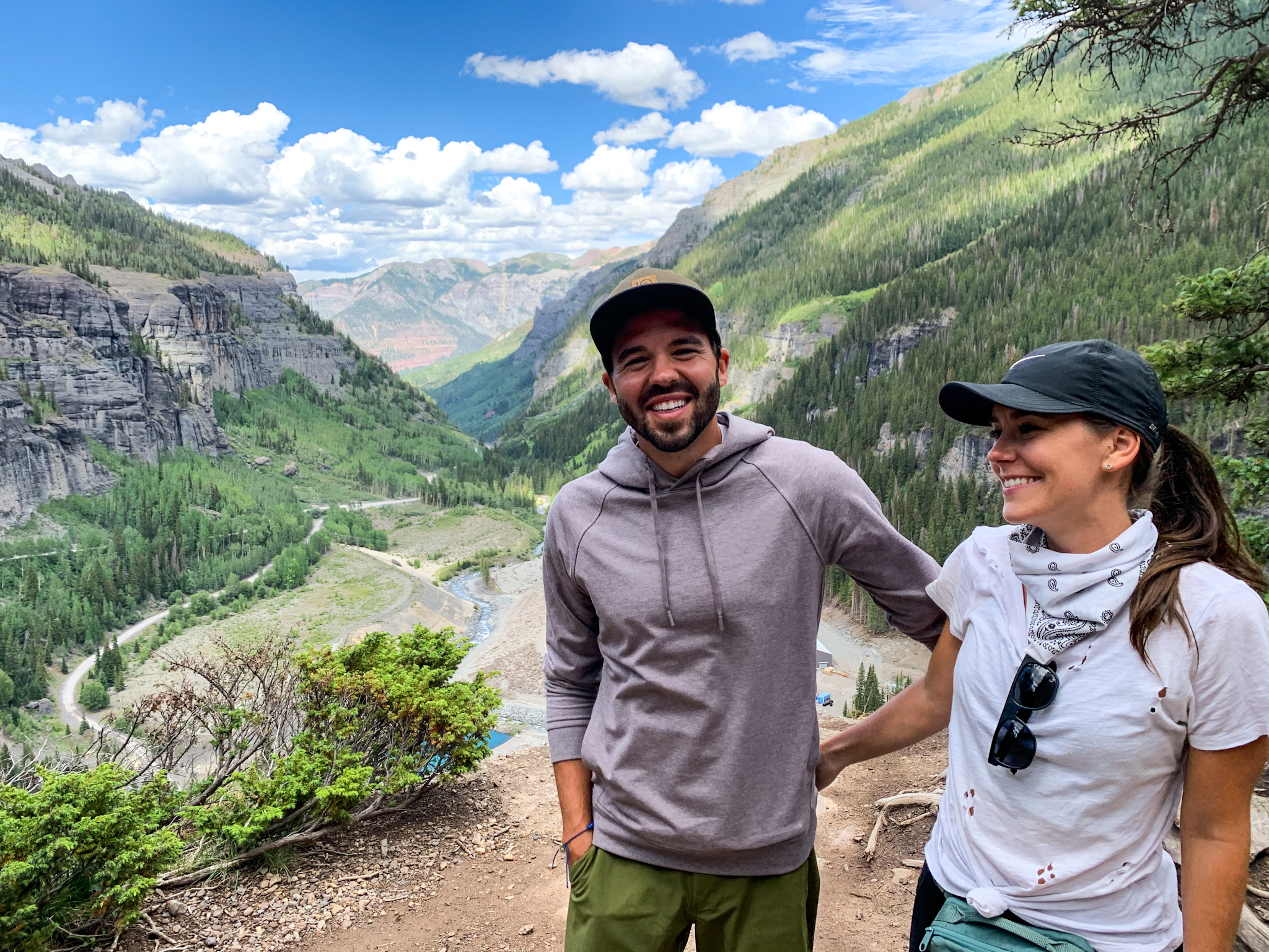 Jason and Dawn smiling for a photo on a ledge in a valley of mountains and trees.
