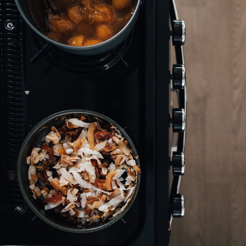 The apricot sauce cooking down on the stove alongside a bowl of toasted coconut flakes and dried fruit. 
