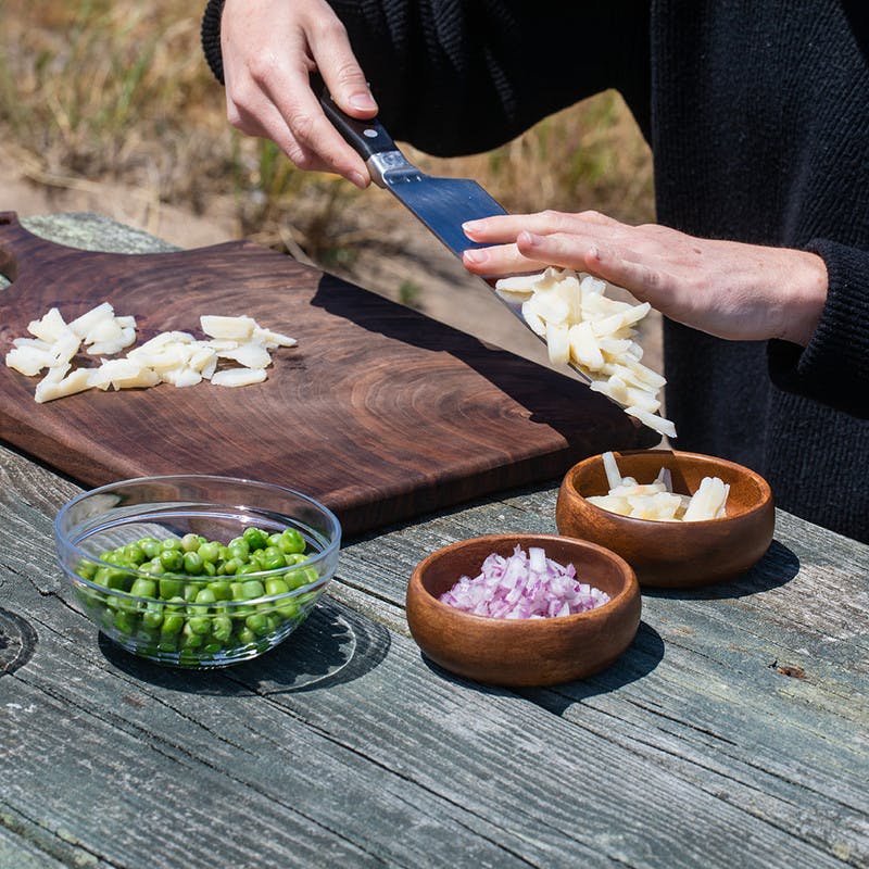 Small bowls on picnic table filled with chopped onion, water chestnuts, peas and cashews on a cutting board.