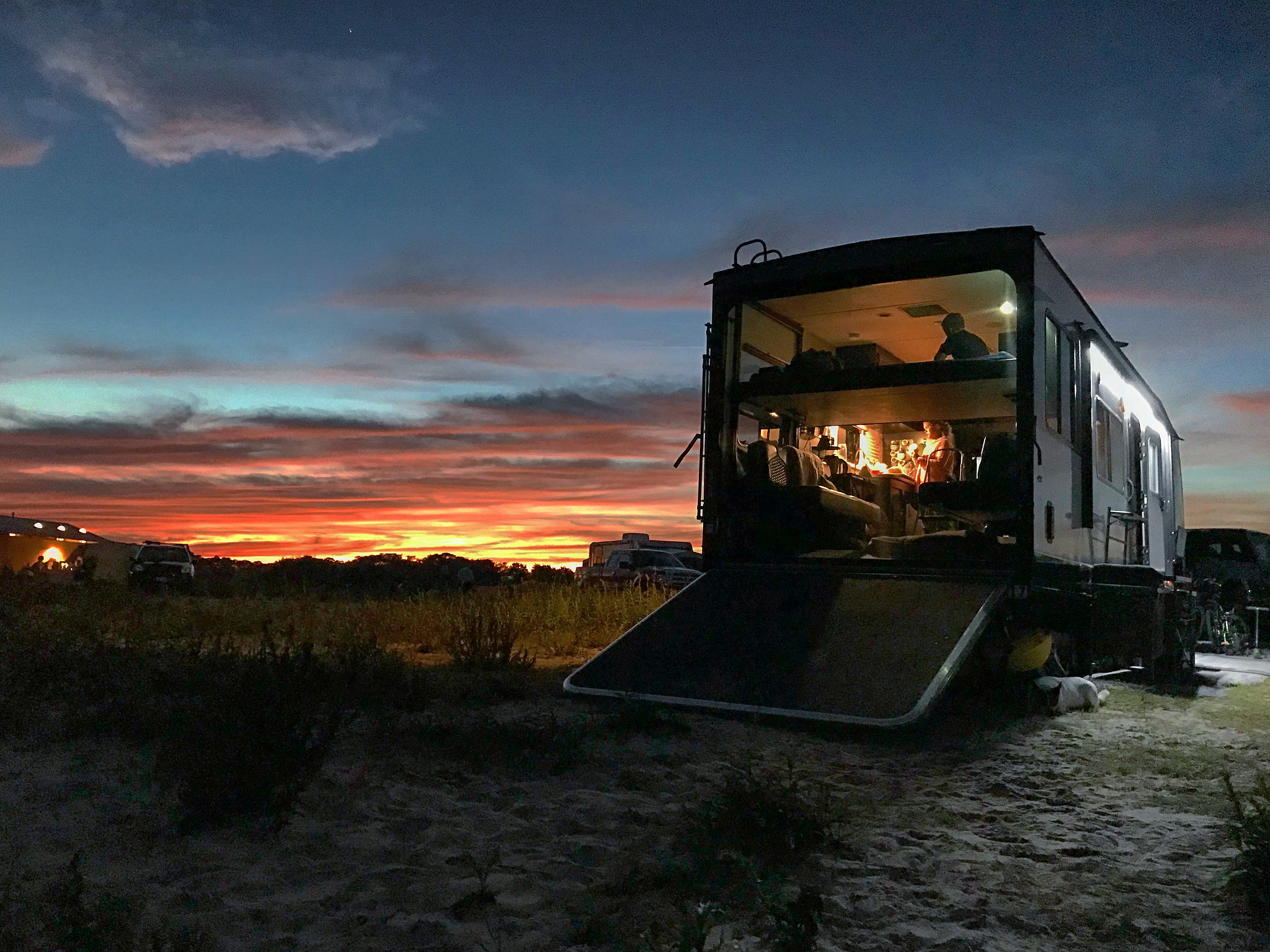 A rainbow sunset over a Toy Hauler RV that's glowing from within with light. 