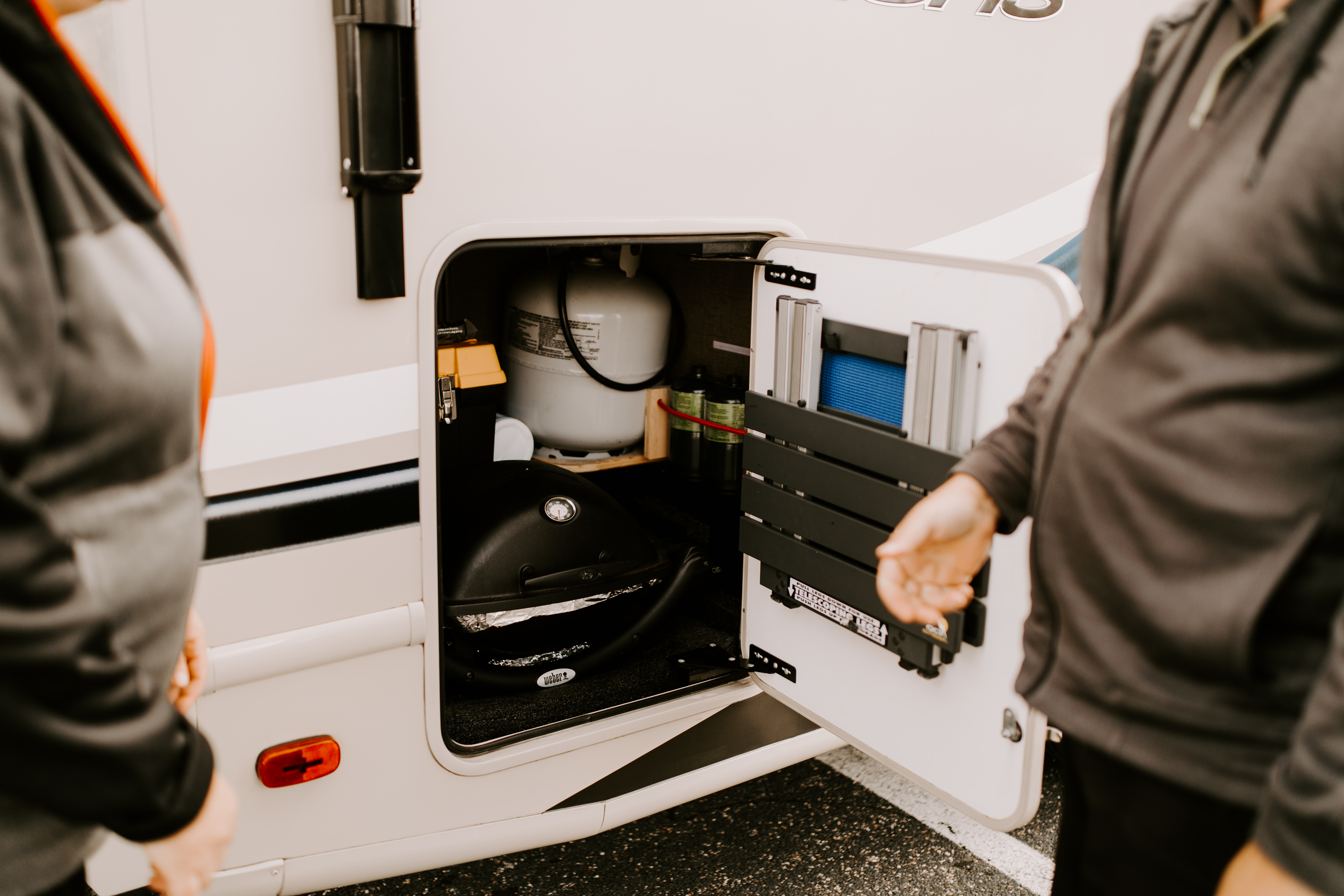 Two people standing outside an open cubby on the exterior of an RV.