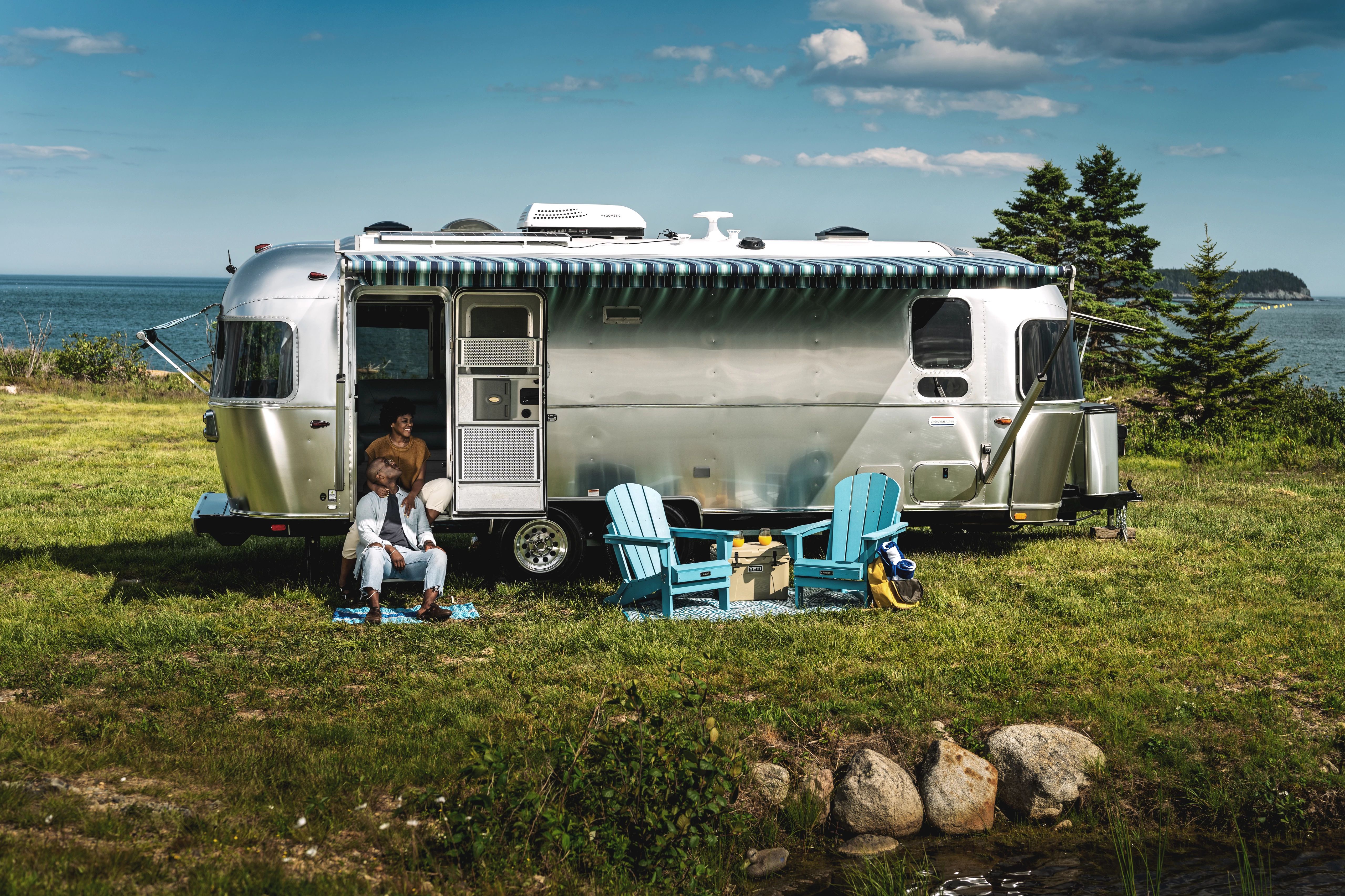  A couple sits on the steps of the doorway of an Airstream travel trailer