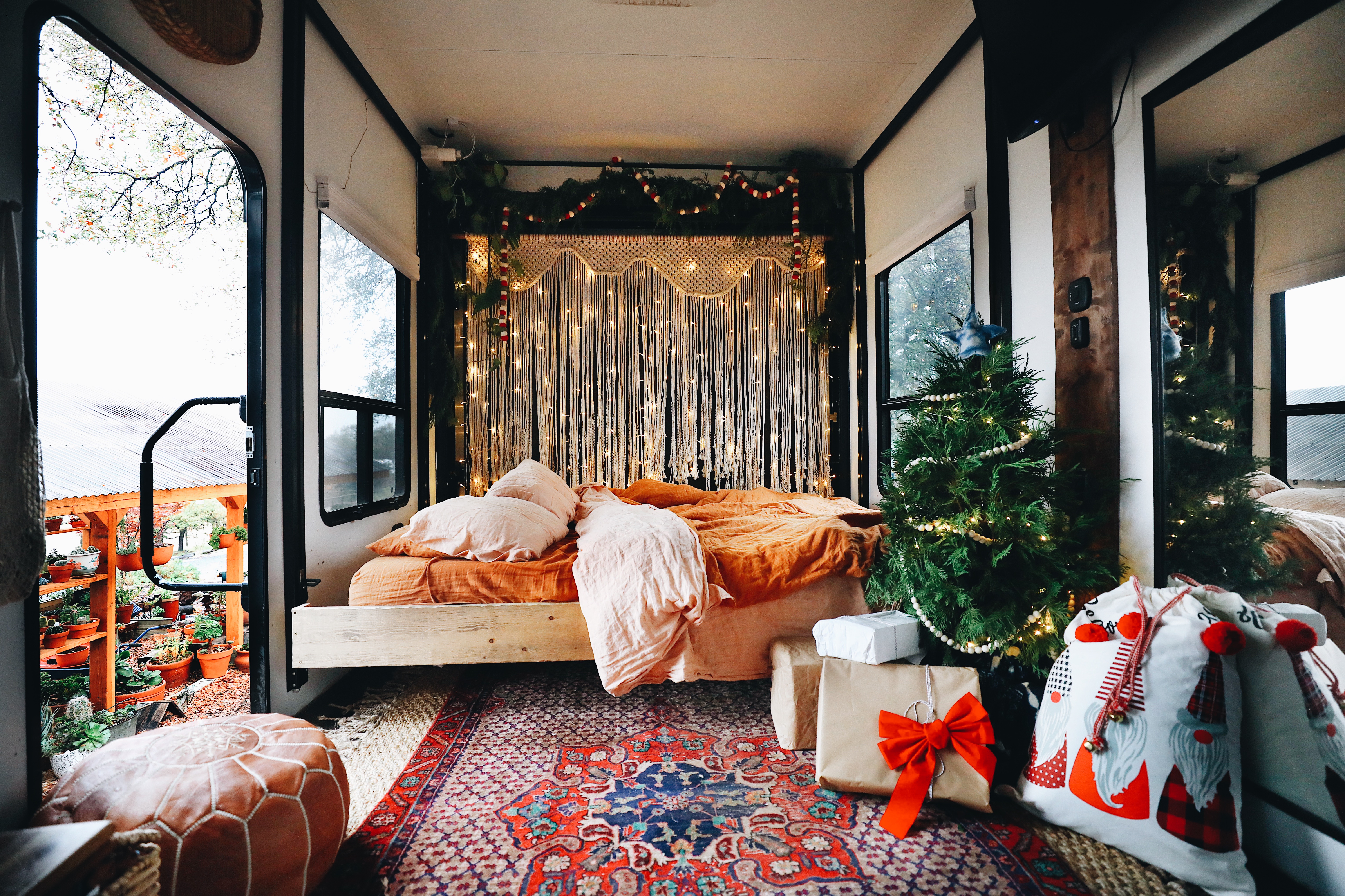 A small Christmas tree surrounded by gifts and lights, nestled in the master bedroom of an RV. 