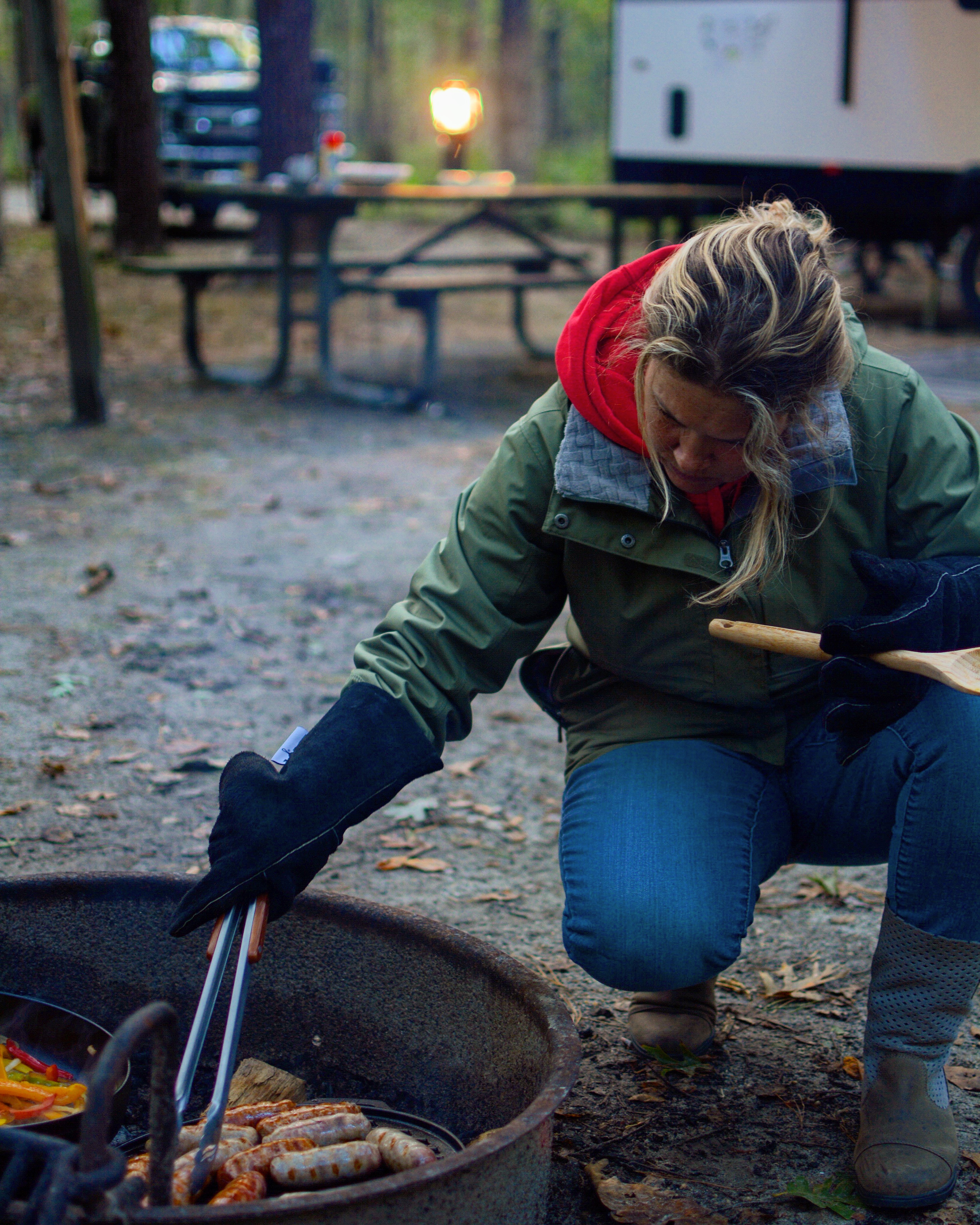 A woman roasting sausages at a campground fire pit. 