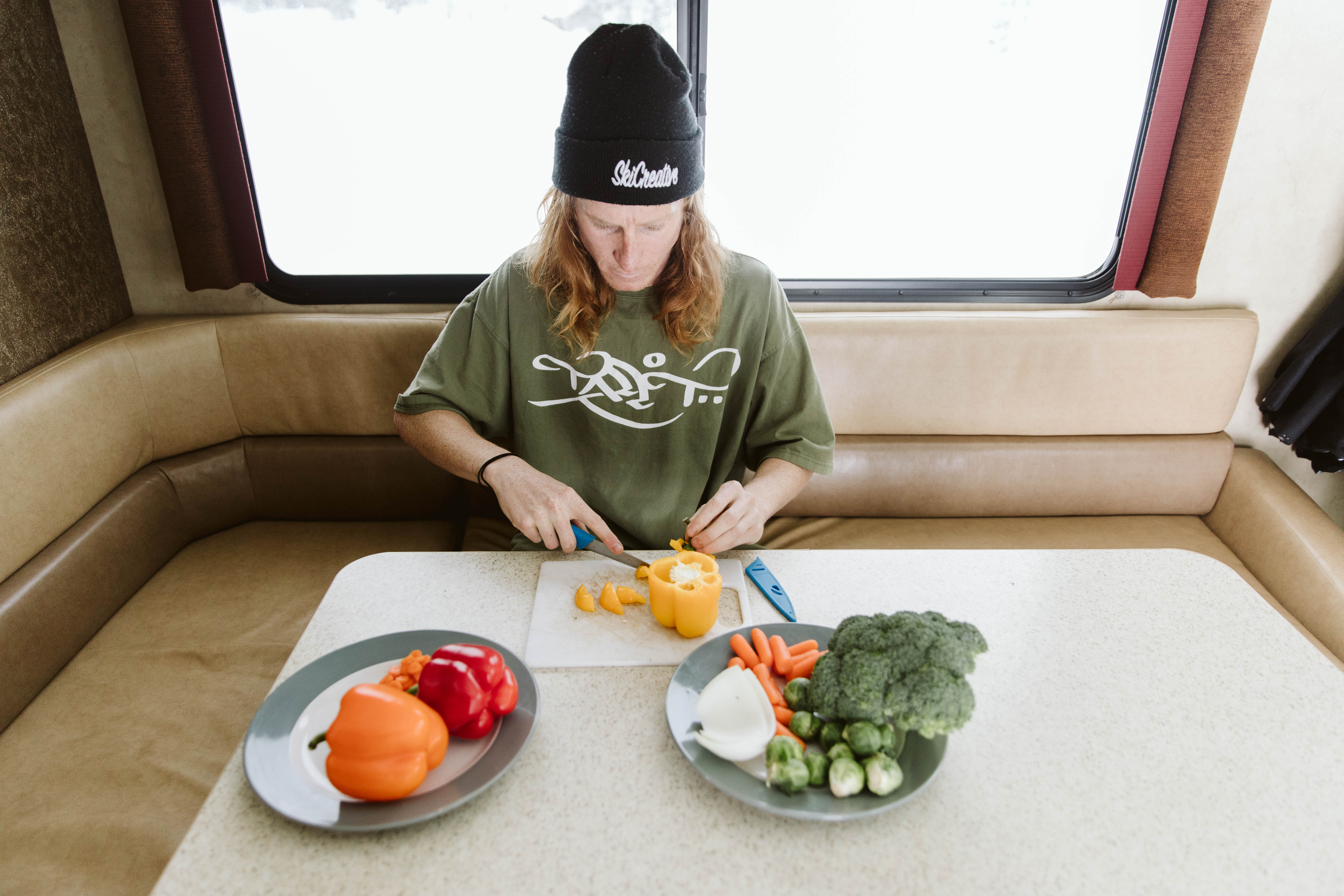 Ryan Barrick sits in Thor Class A motorhome chopping vegetables by snowy window.