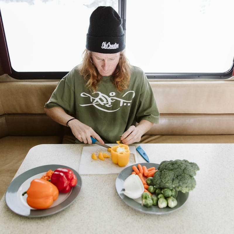 Ryan Barrick sits in Thor Class A motorhome chopping vegetables by snowy window.
