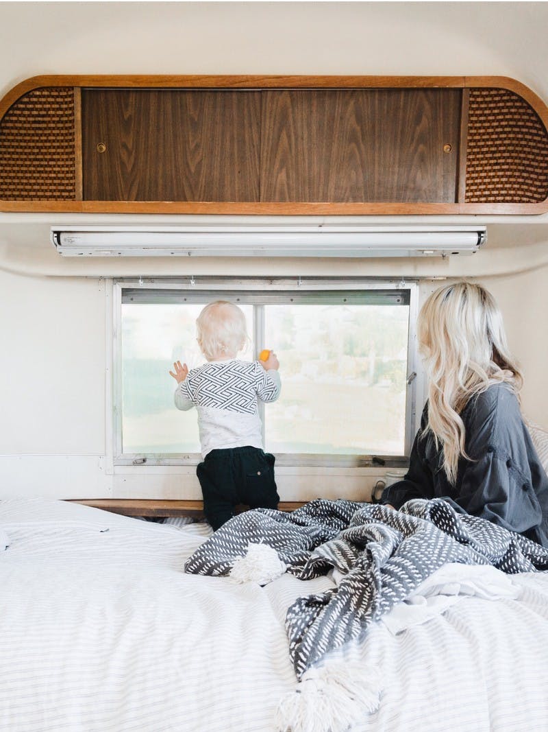 A woman and small child snuggled in blankets in an RV bed look out the window at a beautiful view