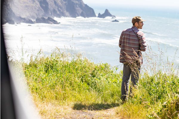 Man with beard stands outside of RV door and looks out onto the Pacific Ocean off of the Pacific Coast Highway in Southern Oregon.