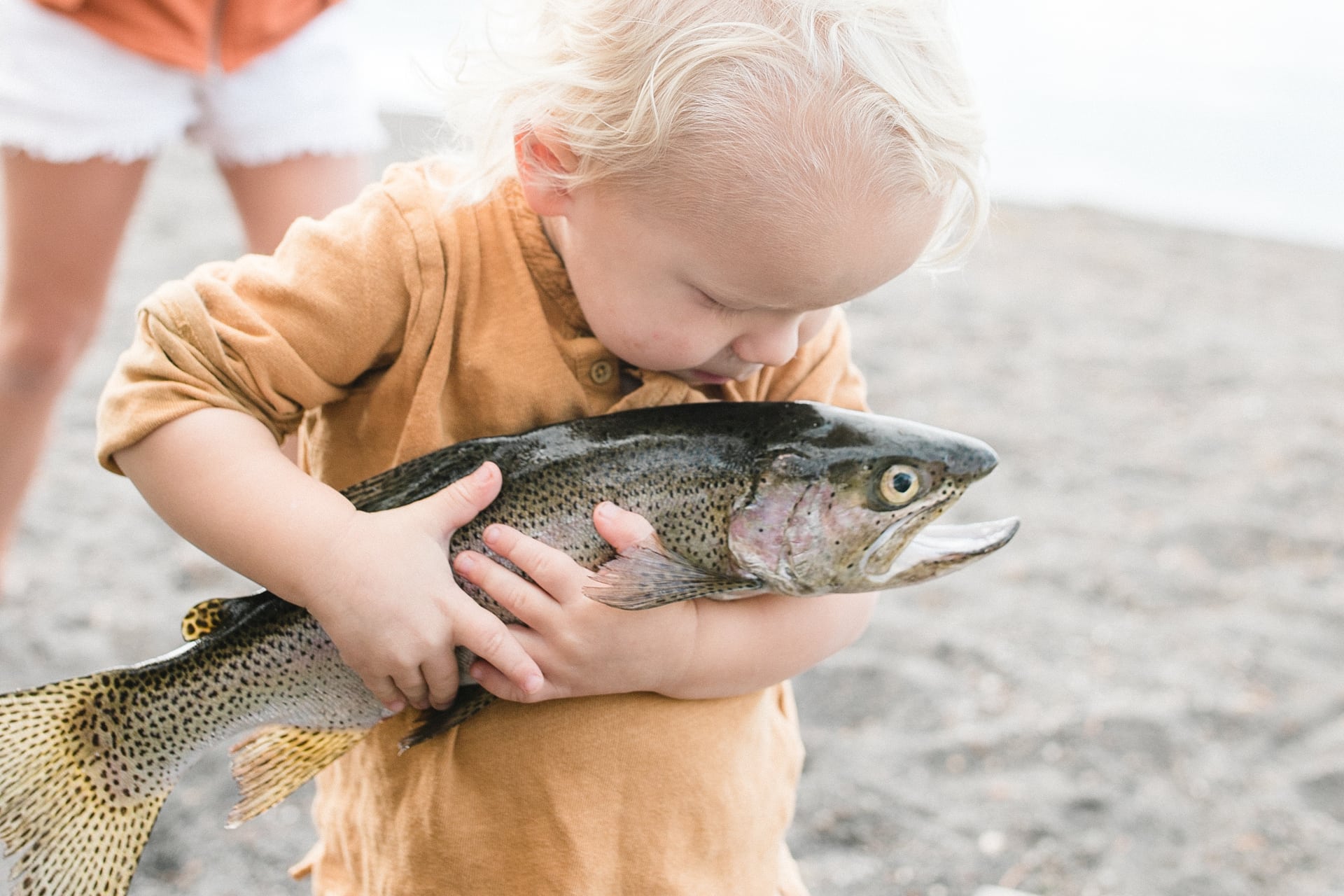 Young toddler holding large fresh trout on shore
