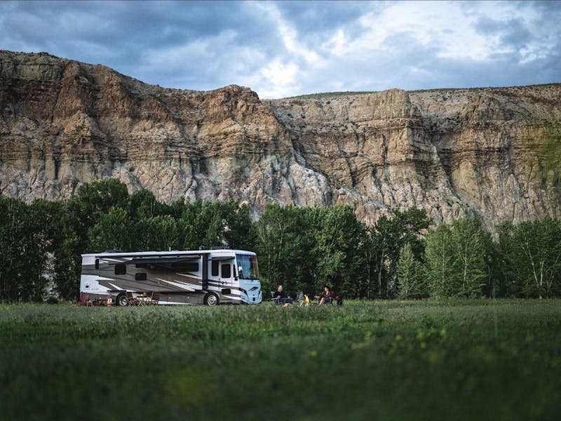 A Tiffin Allegro Red Class A motorhome parked in a field next to a rocky cliffside.