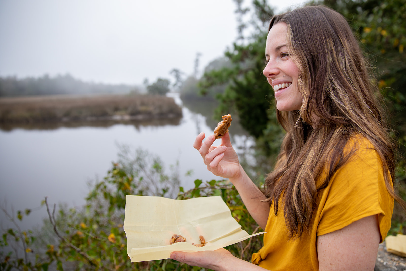A woman smiling and eating a fresh praline candy.