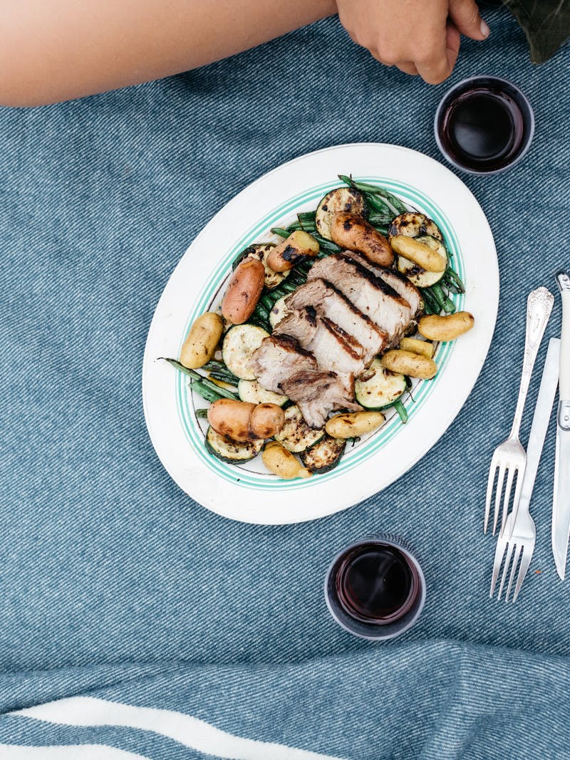 Pork, green beans, and potatoes on a platter with wine and utensils.