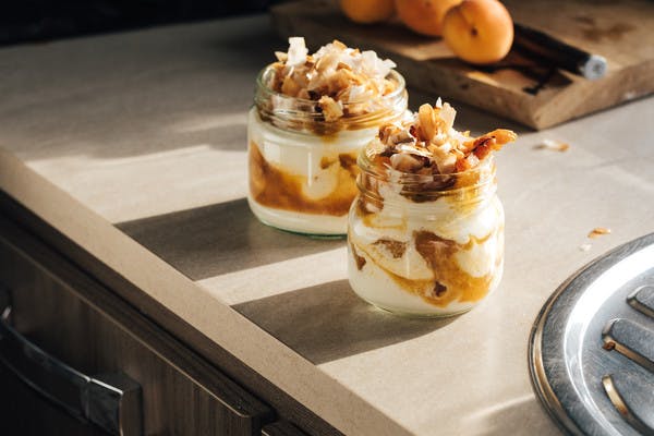 Clear glass jars layered with creamy, white yogurt, golden apricot sauce and toasted coconut flakes.