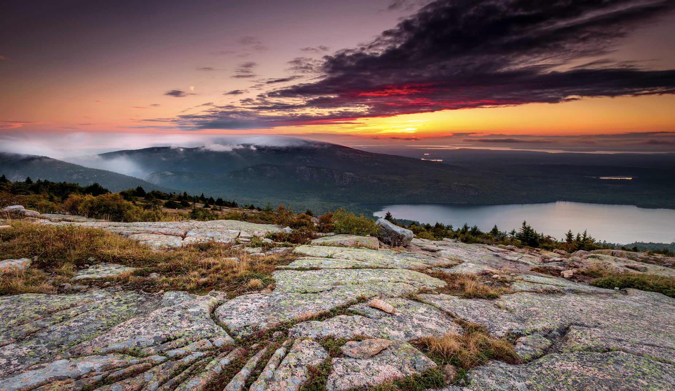 Pink and orange sunset at the top of Cadillac Mountain, overlooking lakes and oceans