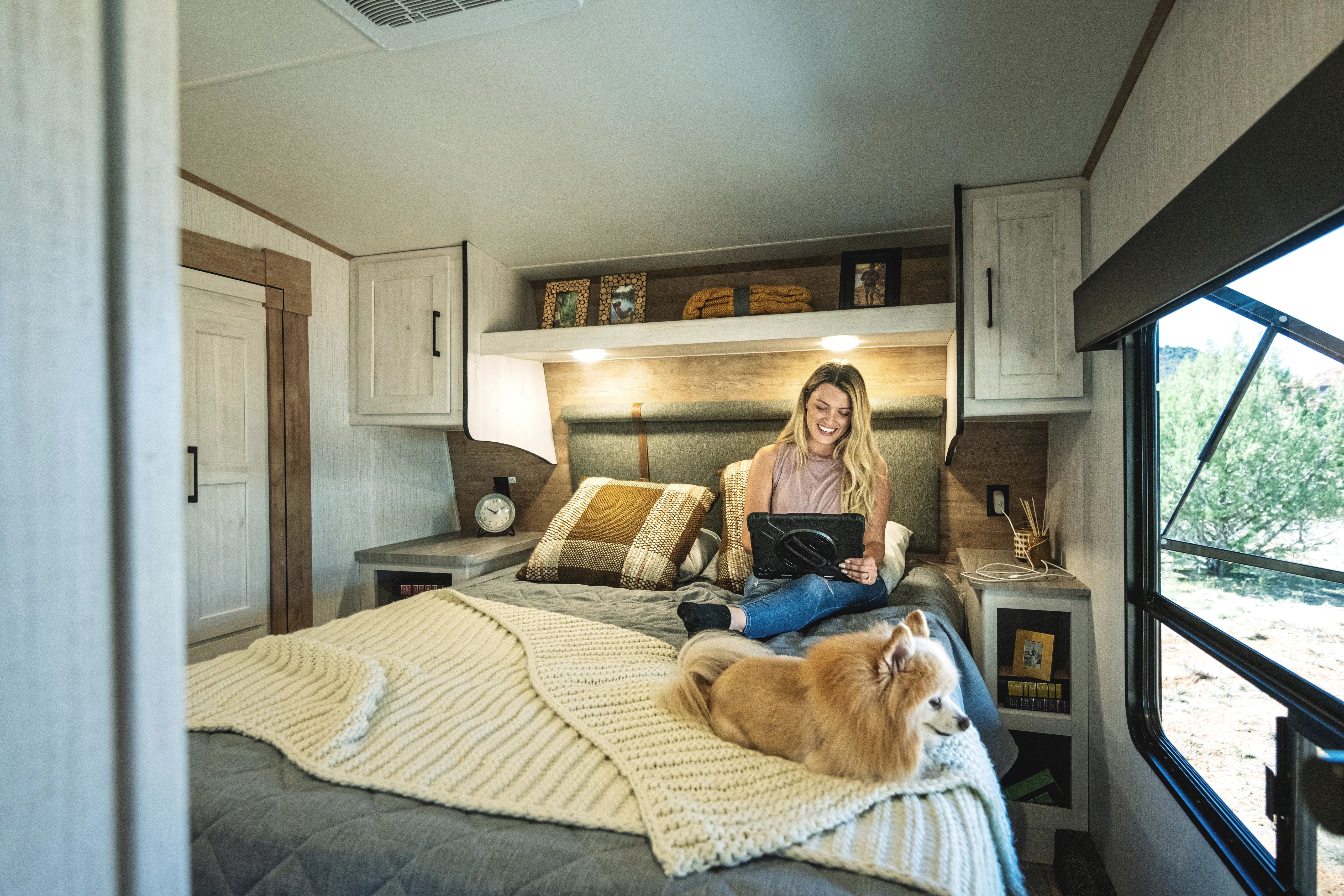 A woman on an Ipad sitting on a bed in a heartland Milestone fifth wheel