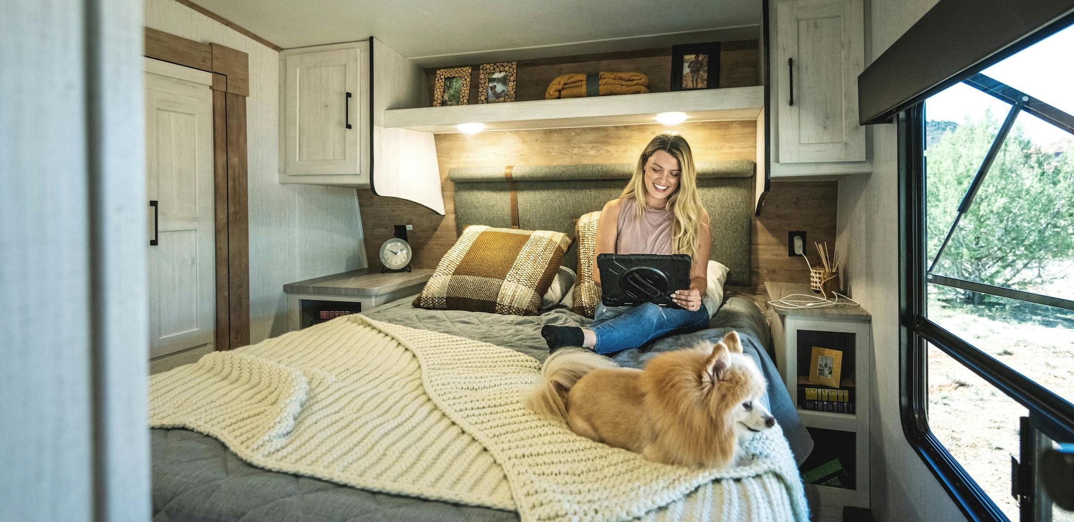 A woman on an Ipad sitting on a bed in a heartland Milestone fifth wheel