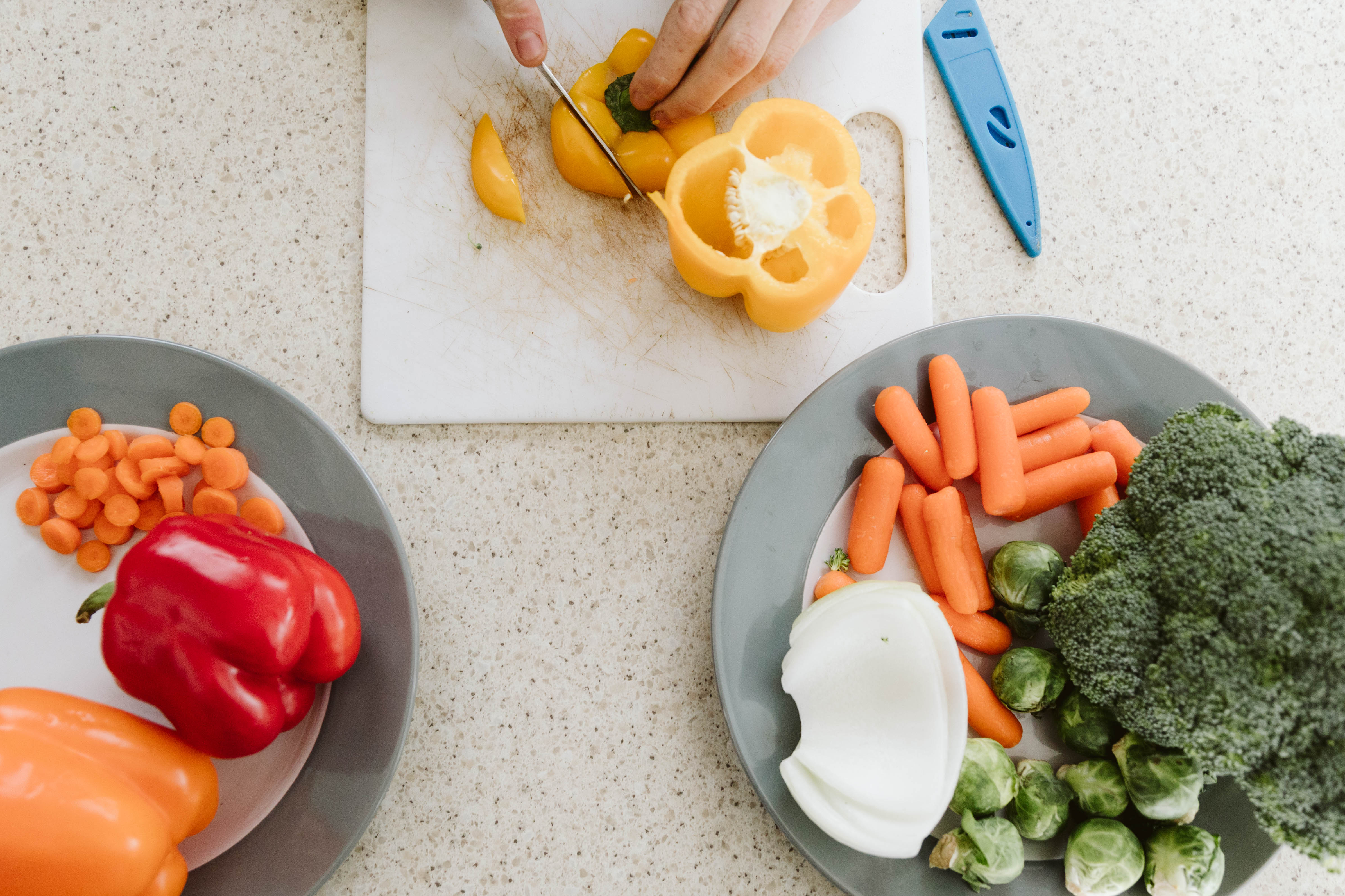 Variety of colorful vegetables on a counter, cutting yellow bell pepper on cutting board