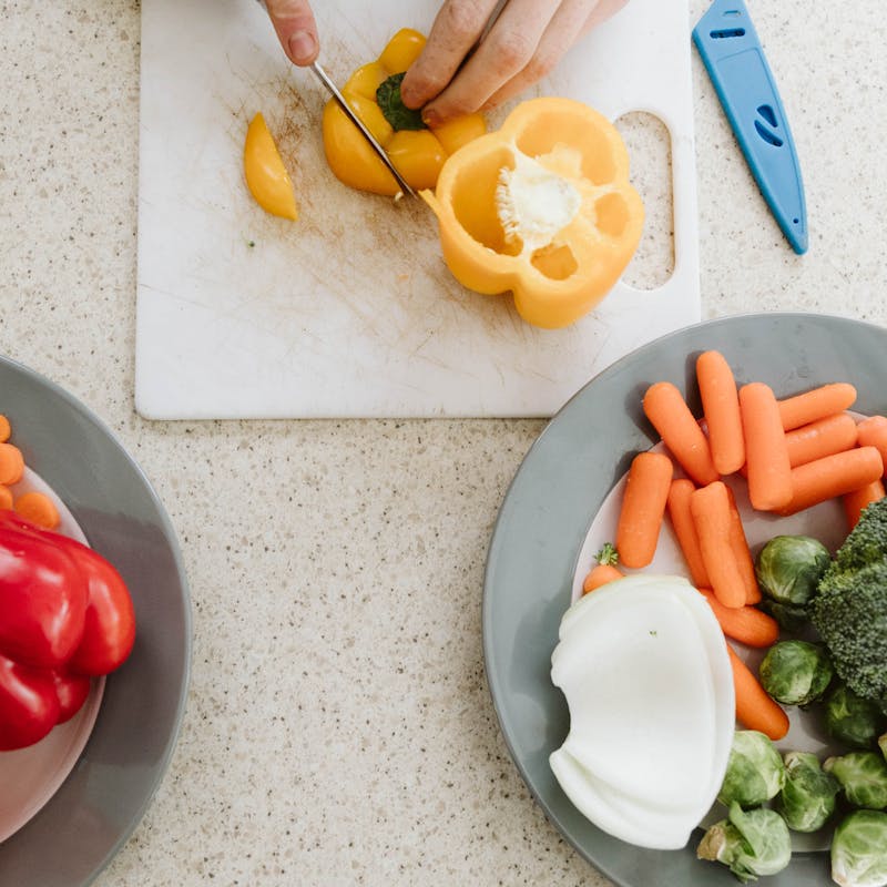 Variety of colorful vegetables on a counter, cutting yellow bell pepper on cutting board