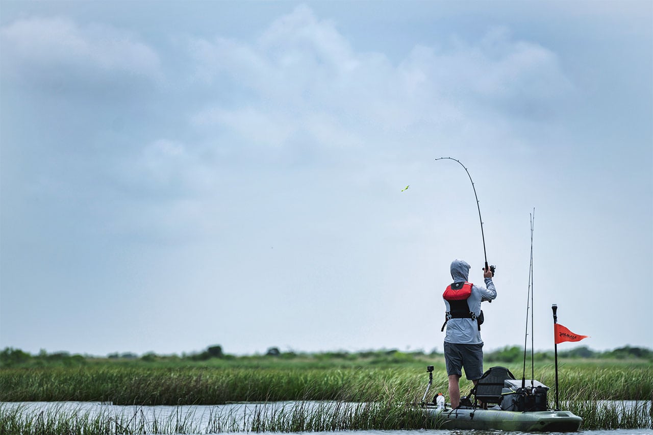 Back of fisherman standing in a kayak casting fishing pole