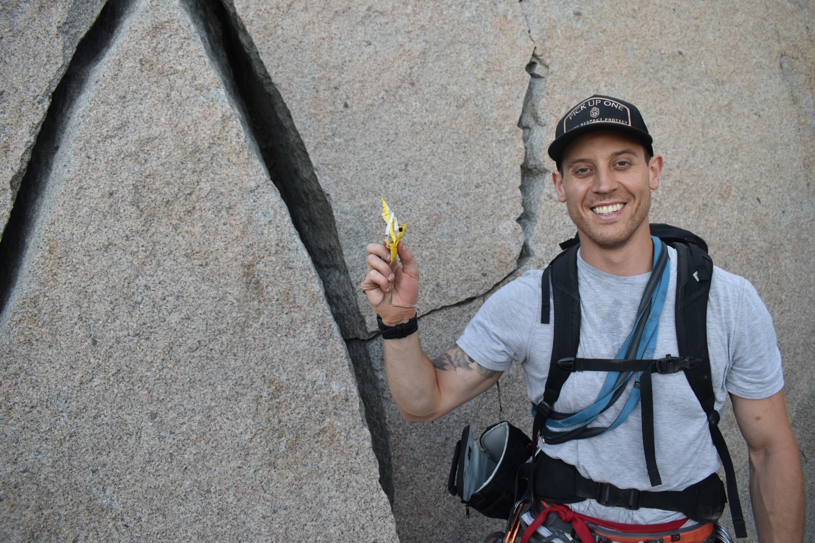 Male rock climber holding up trash in front of a boulder