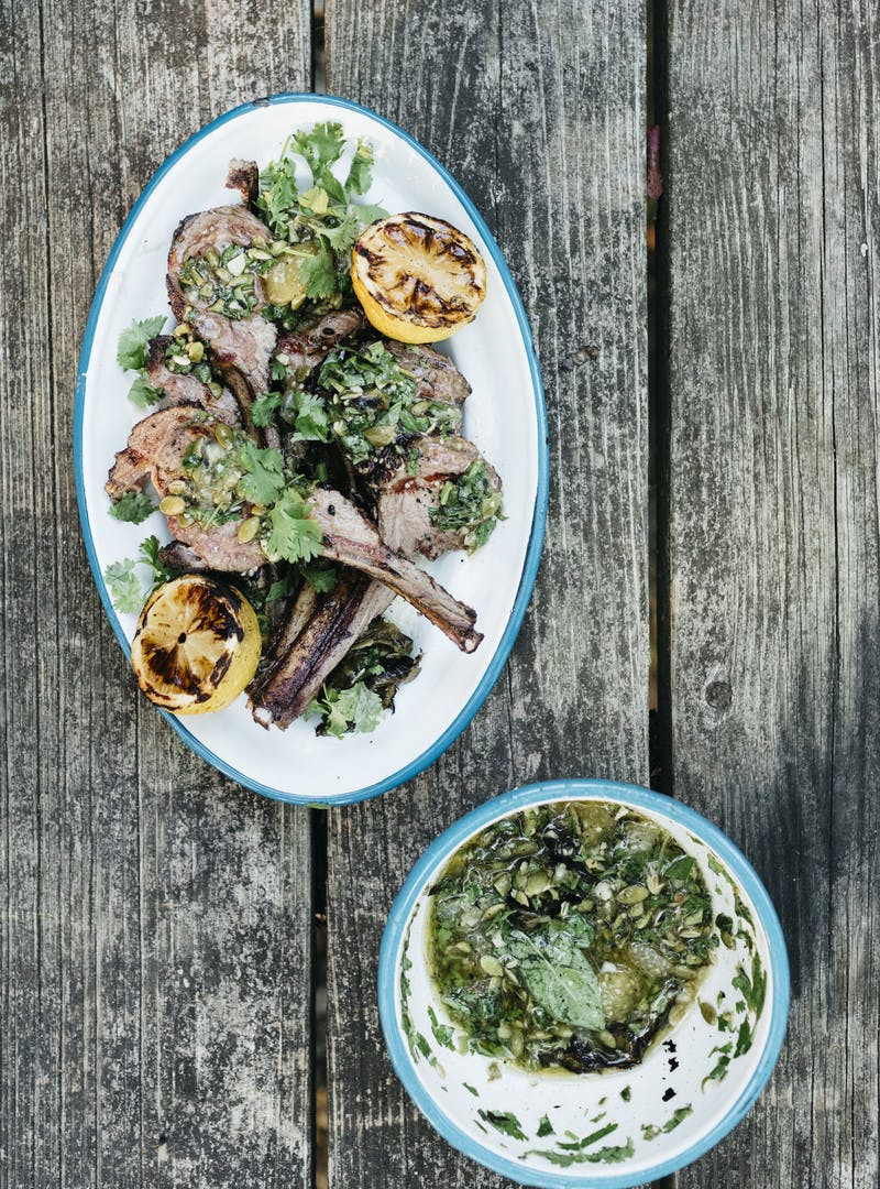 A finished shot of the grilled lamb and tomatillo sauce on a weathered picnic table background.