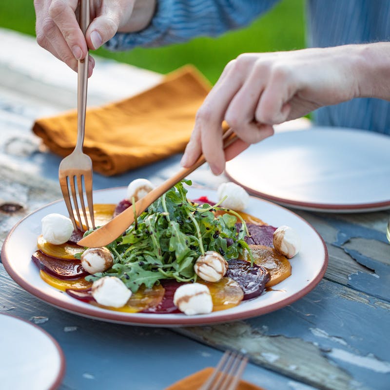 Serving beet, arugula, mozzarella salad into white plate with glass of white wine. 